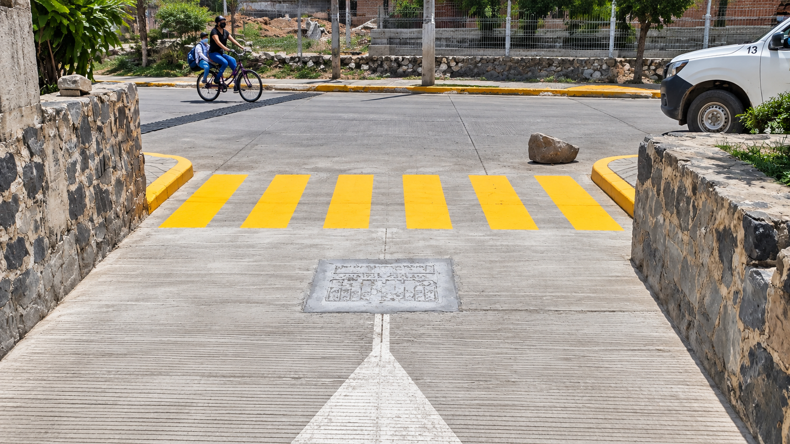 Paso peatonal con franjas amarillas entre muros de piedra.